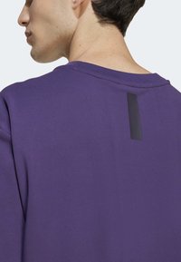 Violetinis džemperis su apykakle, gale esantis matinio juodo atvarto etiketė. Lygus audinys ir laisvas siluetas, tinkamas kasdienei aprangai.