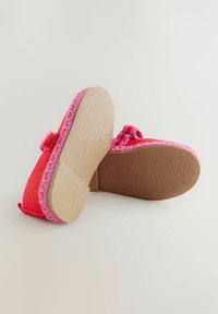 Chaussures en tissu rose avec une semelle en caoutchouc texturé, présentant un accent tressé près de la semelle et une sangle sur le dessus.