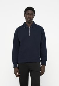 Sudadera azul marino con cremallera, hecha de una mezcla de algodón, con cuello alto, mangas largas y puños acanalados. Diseño simple y limpio.