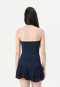 Jūras spēku krāsas strapless bodysuit ar pieguļošu korpusu un daudzslāņu ruffles svārkiem, izgatavots no mīkstas, teksturētas auduma, ar gludu apdari.