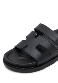 Czarne sandały syntetyczne z dwoma szerokimi paskami z wycięciami, teksturowaną wkładką i grubą, profilowaną podeszwą.