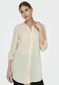 Long-sleeve blouse in soft, lightweight fabric, pale yellow with a button-up front, collarless design, and rolled-up sleeves.