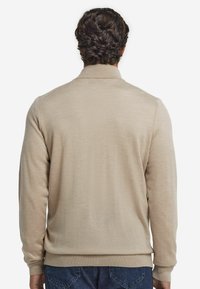 Beige långärmad tröja med krage, tillverkad av mjukt material, med ribbade ärmslut och nederkant. Bakifrån visar den slät textur och enkel design.