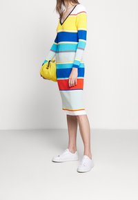 Abito in maglia con maniche lunghe, scollo a V e righe multicolori (giallo, blu, acquamarina, rosso) abbinato a una borsa gialla a texture e sneakers bianche.