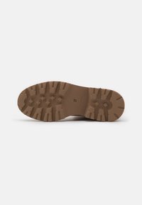 Semelle de chaussure en caoutchouc brun avec des motifs et des rainures profondes pour l'adhérence, marquée de la taille "37" sur une partie plate.