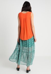 Ærmeløs orange top med rund halsudskæring, kombineret med en flydende grøn mønstret maxinederdel med hvide blomster.