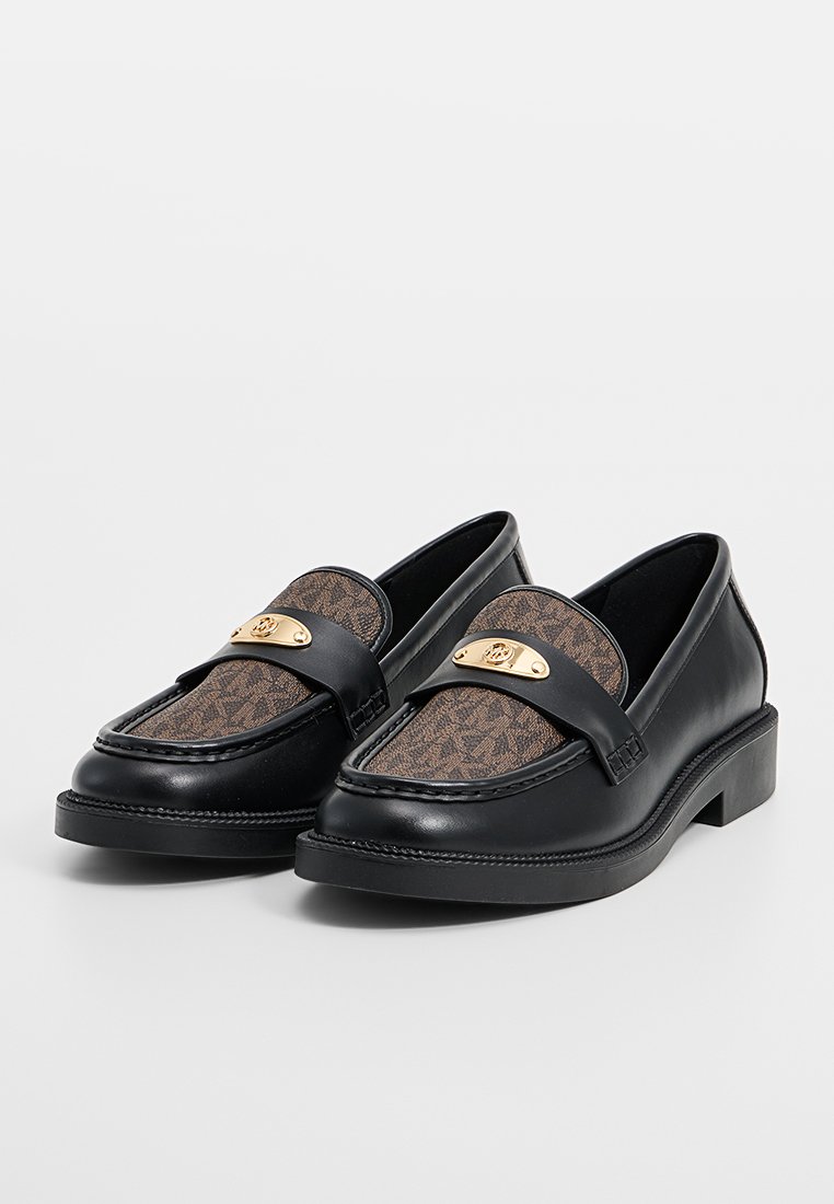 Een paar zwarte leren instappers met bruine gemusterde stofinzetten en gouden metalen logoaccenten op een witte achtergrond.