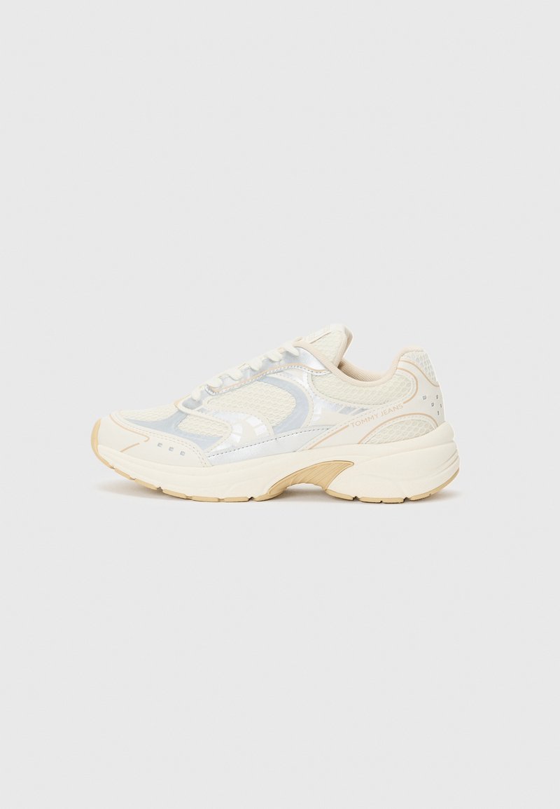 Light cream athletic shoes with a mesh upper, reflective silver accents, and a chunky beige sole. Features lace-up design and logo detail.