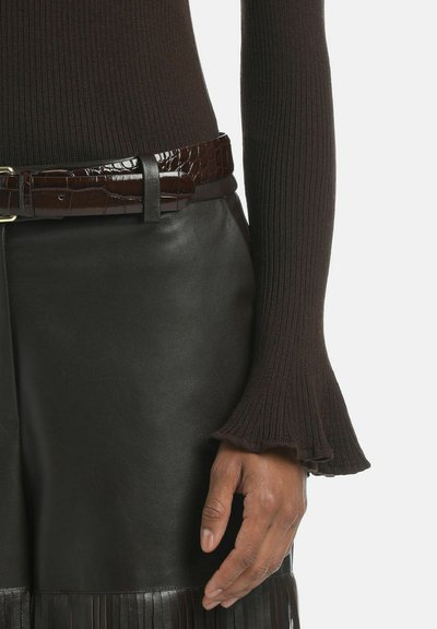 Maglione marrone a coste con maniche a campana abbinato a una gonna in pelle nera con dettagli a frange e una cintura lucida in pelle di coccodrillo marrone.