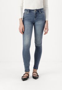 Jeans ajustados en denim azul deslavado, con una cintura de media altura, bolsillos frontales y un sutil efecto de desgaste. Combinados con bailarinas negras.