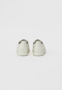 Világosszürke edzőcipők, textúrázott bőrből készült felsőrész, alacsony profil, slip-on kialakítás és sima gumitalpak. Minimalista esztétika és letisztult vonalak.