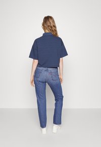 Polo de rayas marinas con mangas cortas, combinado con jeans de mezclilla azules. Diseño limpio con detalles clásicos de bolsillos y zapatillas blancas.