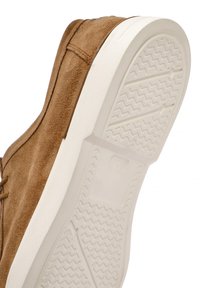 Chaussure en daim marron avec une semelle en caoutchouc blanc. La semelle présente un motif en zigzag pour une meilleure adhérence. L'empeigne a une texture lisse avec des coutures visibles.