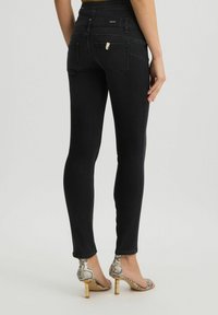 Jeans skinny neri con vita alta, tessuto testurizzato e cuciture a contrasto. Presentano tasche posteriori e un logo vicino alla vita.
