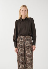 Brown button-up blouse with puffed sleeves; paired with patterned, wide-leg pants featuring intricate beige and black designs.