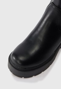 Μαύρη δερμάτινη μπότες μέχρι τον αστράγαλο με στρογγυλή μύτη, υφή και παχύ καουτσούκ πάτο. Ορατή λεπτομέρεια ραψίματος στην επάνω πλευρά.