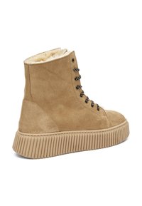 Botas tobilleras de ante marrón con forro de piel sintética, punta redonda, seis ojales metálicos y suela de plataforma acanalada.