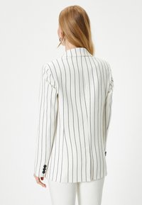 Blazer blanco a rayas con textura, que presenta un ajuste entallado, cierre de un solo botón y puños con tres botones.