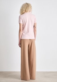 Rosa polo skjorte med korte ermer og en tettsittende passform, kombinert med beige vide bukser, begge på en nøytral bakgrunn.