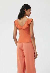 Top naranja con volantes y un diseño en la espalda en forma de V, hecho de tejido suave, combinado con pantalones fluidos de color naranja claro, que ofrecen un ajuste relajado.