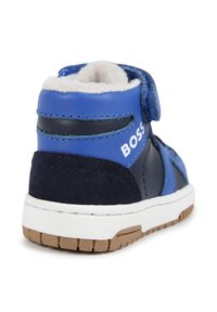 Baskets montantes en cuir bleu et daim marine, avec une sangle velcro ajustable, une semelle en caoutchouc blanche et une doublure en polaire douce.