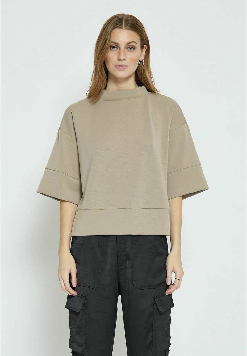Beige top s krátkým rukávem a vysokým výstřihem, s volným střihem a vodorovnými švy, spárovaný s černými cargo kalhotami s kapsami.