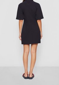 Černé šaty s krátkým rukávem a límečkem, se splývavým střihem a jemným červeným prošíváním. Nosí se s černými a červenými žabkami.