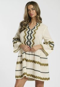 Robe à manches évasées en tissu crème avec des motifs en zigzag en olive et noir, dotée d'un décolleté en V et d'accents texturés.