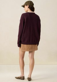 Pull en maille bourgogne, jupe mini en velours côtelé beige, casquette à imprimé léopard et ballerines en serpent. Design simple, textures chaudes, tenue décontractée.