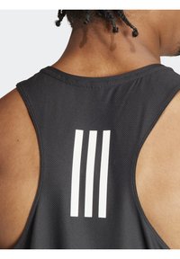 Débardeur de sport noir en tissu texturé, avec de larges emmanchures et trois bandes verticales blanches au dos.