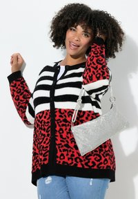 Schwarz-weiß gestreifter Cardigan mit einem rot-schwarzen Leopardenmuster. Verfügt über einen Knopfverschluss, gerippte Bündchen und wird mit einer silbernen Handtasche kombiniert.