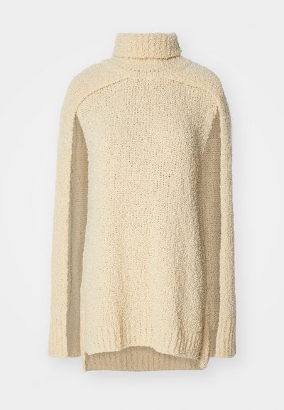 Beige, chunky-knit sweater with a high collar, long sleeves, and side slits. Textured surface with a soft, cozy appearance.