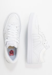 Vita sneakers med en slät läderövre, perforerad detaljer, snörning och en texturerad gummisula. Logotyp synlig på innersulan.