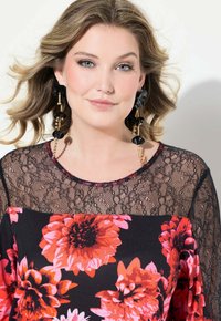 Svart spetsblus med blommönster; har livfulla röda och rosa blommor, rund halsringning med beadade detaljer och hängande svarta örhängen.