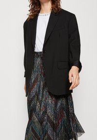 Černé sako s jedním knoflíkem, spárované s bílým topem s drahokamovým výstřihem a barevnou skládací sukni se zigzagovým vzorem.