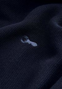 Țesătură tricotată de culoare bleumarin închis, cu o textură netedă, care prezintă un design brodat cu un homar gri deschis. Reflexia subtilă adaugă un interes vizual. 
