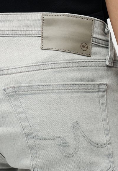 Τζιν denim ανοιχτό γκρι με απαλή υφή, με δερμάτινο μπαλώμα στη μέση και διακριτικό σχέδιο τσέπης με ραφές.