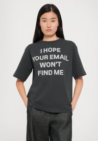 Sort bomulds T-shirt med korte ærmer og stort gråt tekst: "JEG HÅBER DIN EMAIL IKKE FINDER MIG." Afslappet pasform, rund halsudskæring.