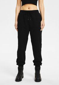 Czarne spodnie dresowe o luźnym kroju, z elastycznym pasem, sznurkiem do ściągania i zwężanymi mankietami, zestawione z czarnymi botkami na sznurowadła.