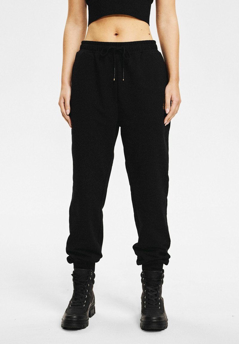 Czarne spodnie dresowe o luźnym kroju, z elastycznym pasem, sznurkiem do ściągania i zwężanymi mankietami, zestawione z czarnymi botkami na sznurowadła.