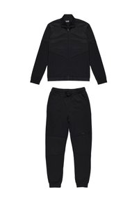 Tuta nera composta da una giacca con zip e dettagli in rete, abbinata a pantaloni con elastico in vita e pannelli testurizzati.