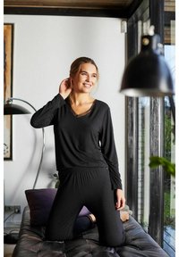 Set di abbigliamento lounge nero composto da maniche lunghe, scollo a V con bordo in pizzo e pantaloni a vestibilità rilassata con vita elastica, su un divano.
