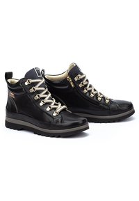 Bottines noires en cuir avec une surface texturée, œillets dorés, lacets beiges et une semelle en caoutchouc avec un léger talon.