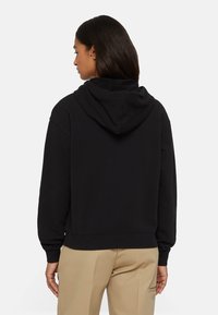 Felpa nera con cappuccio, dotata di polsini e orlo a costine, caratterizzata da una consistenza morbida. Dettagli di cucitura visibili e vestibilità comoda con vista posteriore.