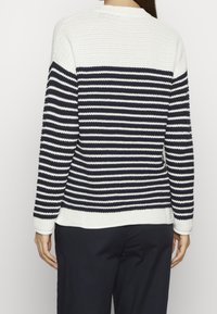 Vit och marinblå randig tröja med strukturerad stickning, rund halsringning, långa ärmar och ribbade muddar. Har en avslappnad passform med en något rundad nederkant.