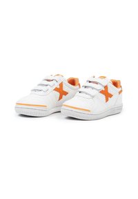 Zapatillas deportivas blancas para niños con un logo naranja en forma de "X" y correas de velcro sobre un fondo blanco.