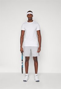White short-sleeve t-shirt, gray athletic shorts, and white sneakers with blue accents. Holding a tennis racket, wearing a white headband.