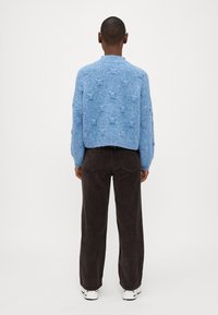 Suéter de punto esponjoso azul claro con puntos texturizados, dobladillo y puños acanalados, combinado con pantalones de pana marrón oscuro y zapatillas blancas.