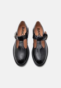 Γυαλιστερά μαύρα δερμάτινα παπούτσια Mary Jane με Τ-ιμάντα και ασημένια αγκράφα, ταμπά εσωτερικές σόλες με το όνομα επωνυμίας "BIANCO", φωτογραφημένα από πάνω σε λευκό φόντο.