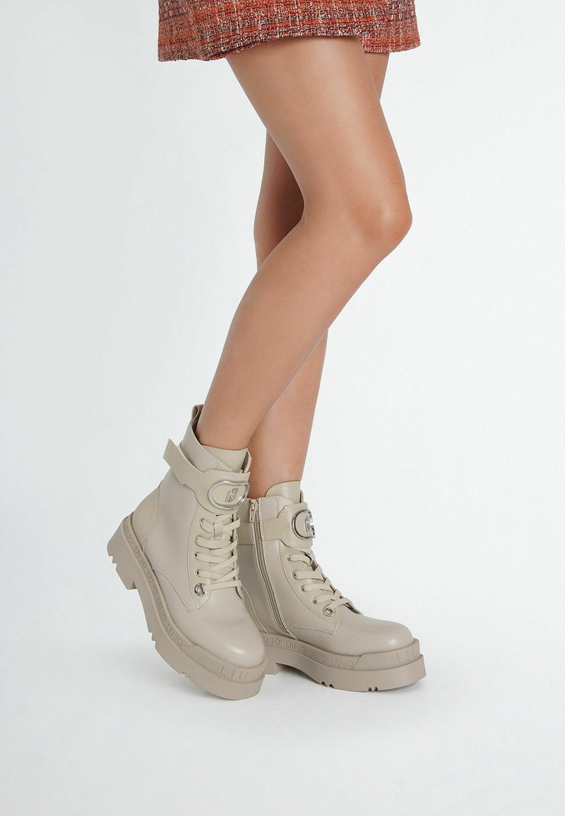 Beige enkellaarzen van glad leer, met een ritssluiting, veters en een verstelbare band, en een dikke, gestructureerde platformzool.